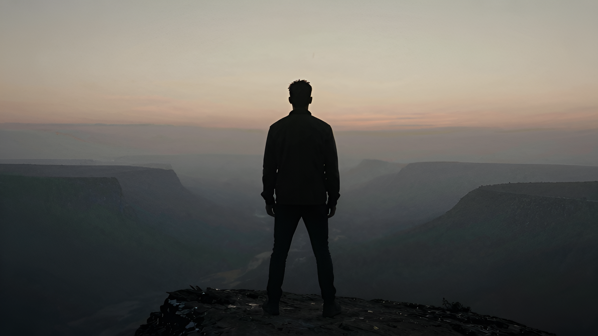Silhouette of a man standing on a cliff edge at dawn
